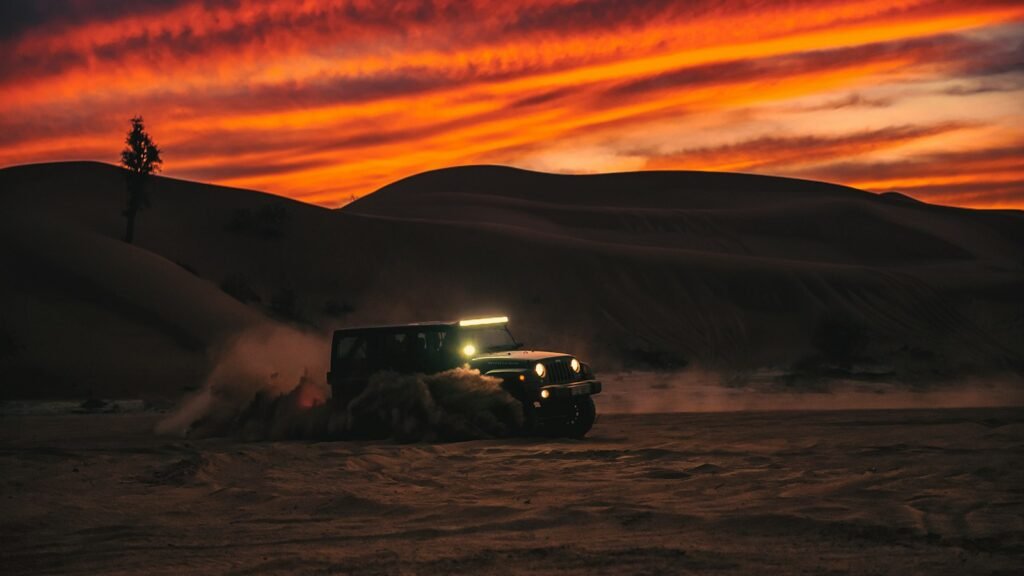 Off-road vehicle driving across desert sand at sunset